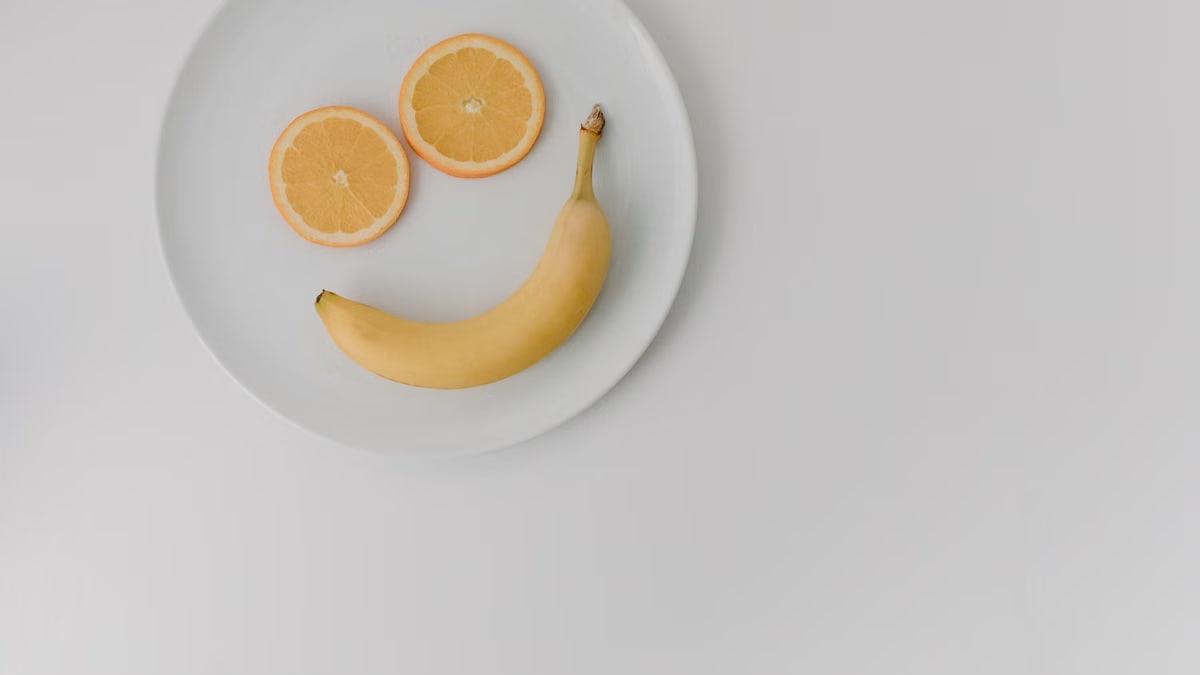 A playful arrangement of banana and orange slices forming a smile on a white plate.